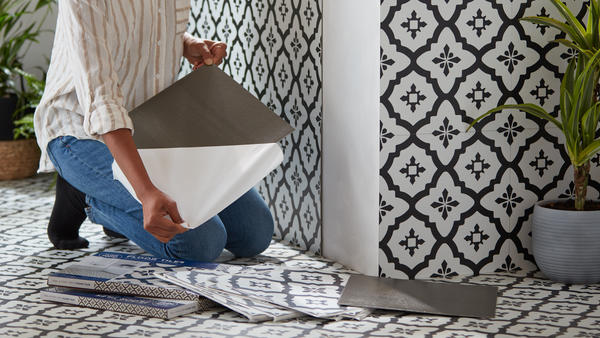 A woman peeling the backing off a large black and white tile in a bathroom