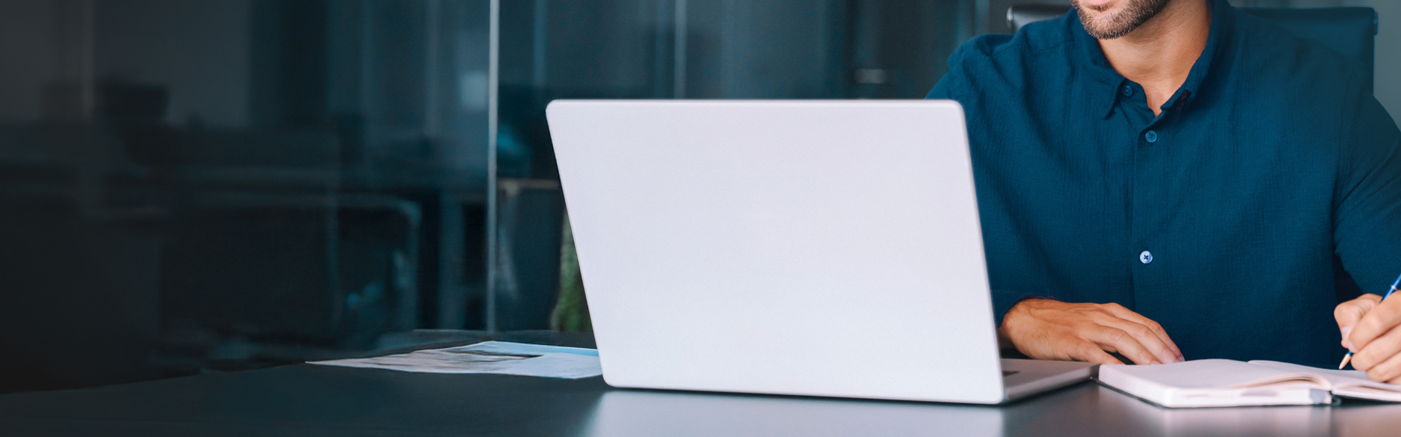A professional working at desk with laptop and documents in modern office.