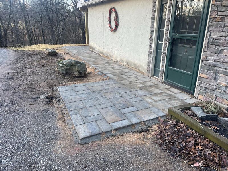 Stone walkway installed along house exterior leading to entrance. The structured paver layout enhances accessibility and curb appeal, showcasing professional hardscaping work designed for durability, drainage, and seamless integration with surrounding landscape features.