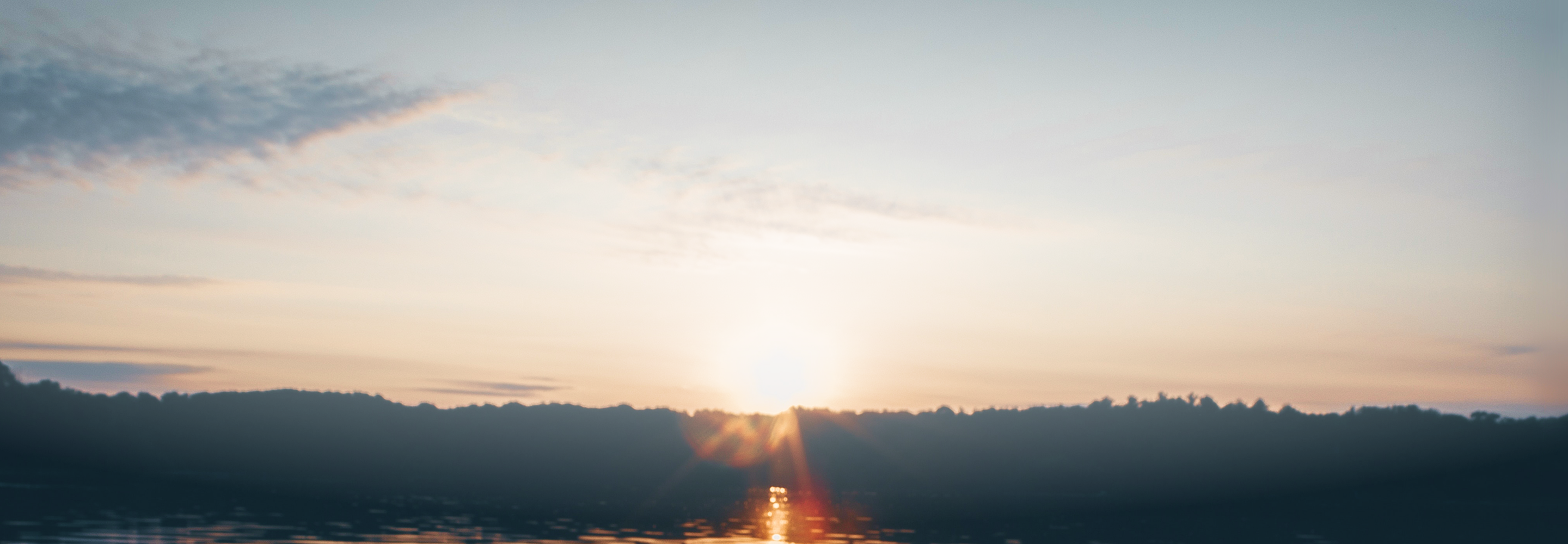 Sun setting over a silhouetted forest surrounding a lake.
