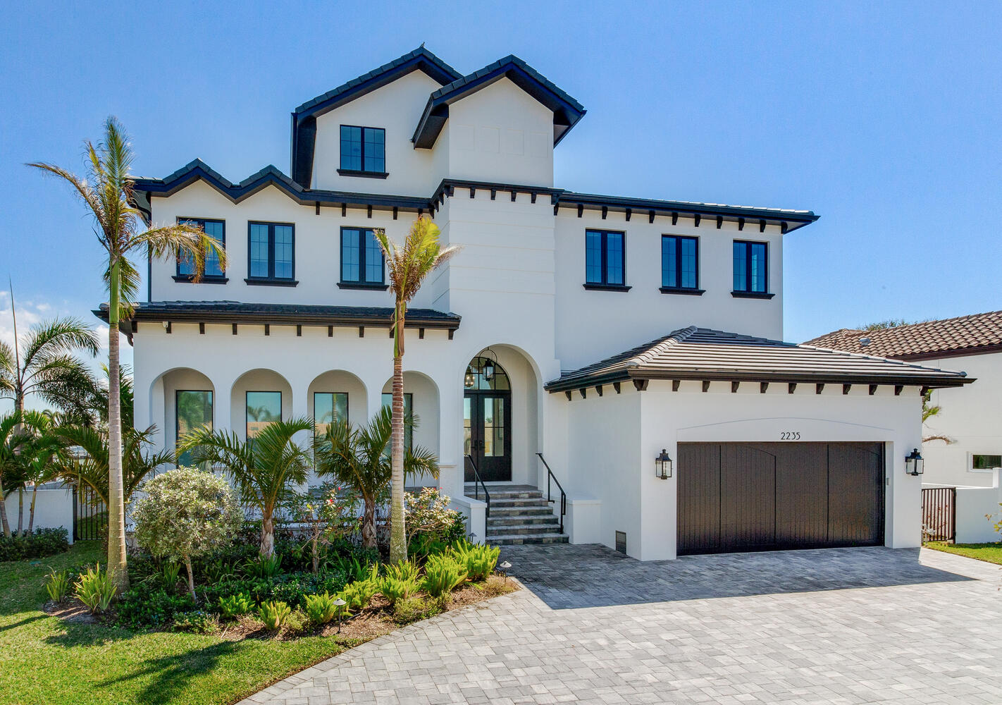 Mediterranean-inspired custom home exterior with arched windows, tile roof accents, palm landscaping, and an elegant coastal curb appeal.