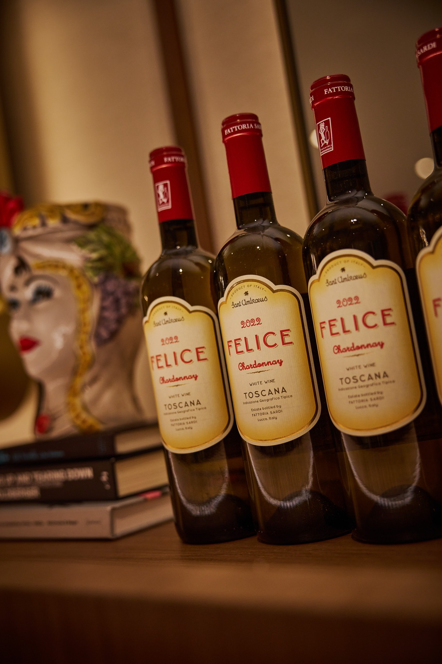 A row of 2022 Felice Chardonnay wine bottles displayed next to a decorative ceramic Moor&rsquo;s head vase in an upscale dining setting.