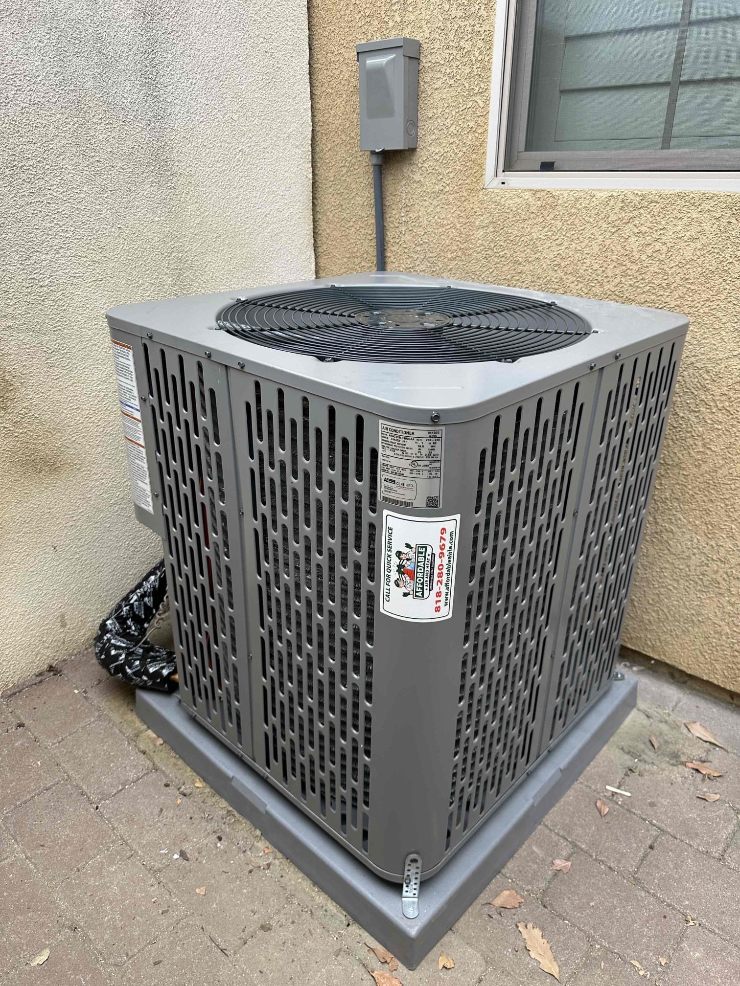 A newly installed air conditioning condenser unit with an Affordable Heating and Air service sticker, positioned on a concrete pad outside a residential home in Ventura County.