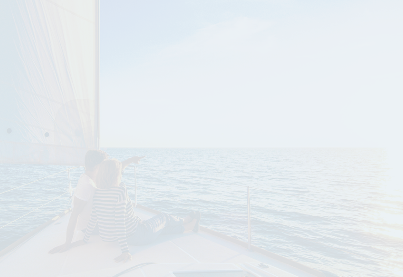 A couple looking out at the ocean from the bow of a sailboat at sunset.