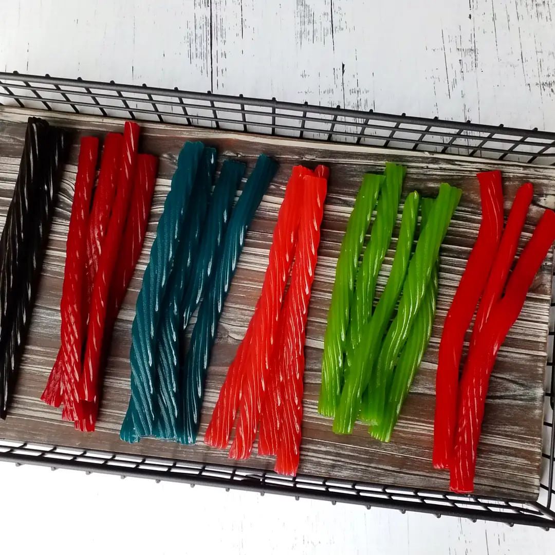 The Licorice Guy's full range of licorice flavors displayed on a rustic wooden tray, showcasing the variety of vibrant colors from traditional black and red to blue raspberry, cinnamon, and green apple.