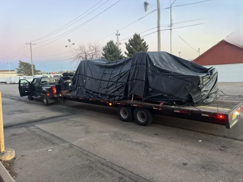 Heavy cargo covered with weatherproof tarps is securely strapped to a flatbed trailer, demonstrating 
