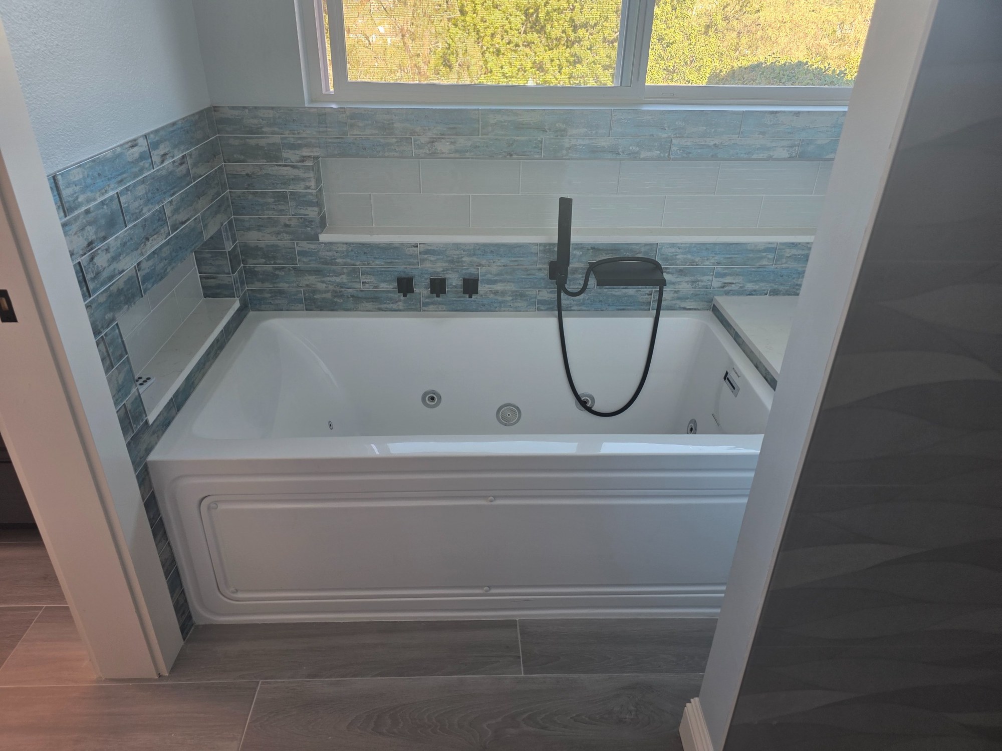 Bathroom remodel featuring a soaking tub, tiled surround, window, and handheld fixture. 