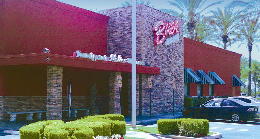 The exterior of Buca di Beppo Anaheim showcases the front parking lot and the signature red and green building with a Buca sign at the front.