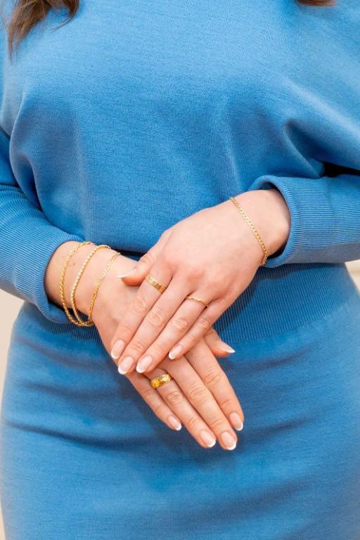 Delicate gold-tone bracelets and textured rings add a warm accent to a blue knit outfit at Eliana Curated. Explore jewelry for stacking, layering and everyday styling in Old Town Alexandria, Virginia.