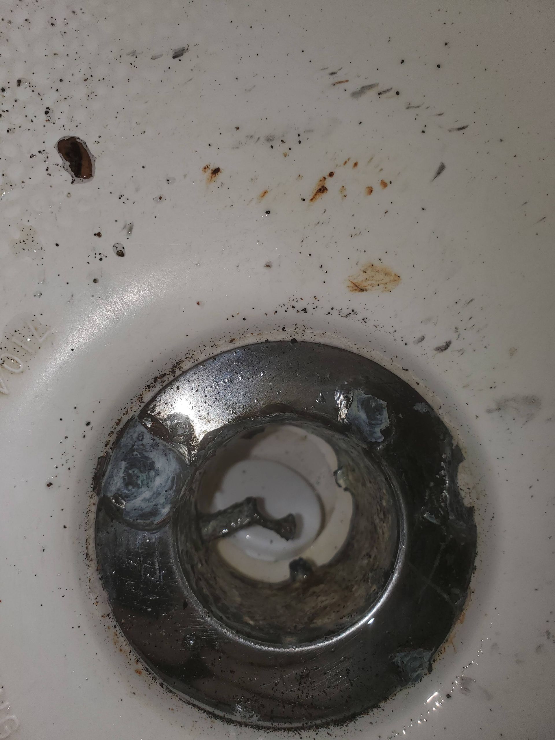 Close-up of a dirty sink drain with visible rust, debris, and residue buildup around the metal opening, indicating poor drainage conditions and need for professional cleaning and maintenance service.