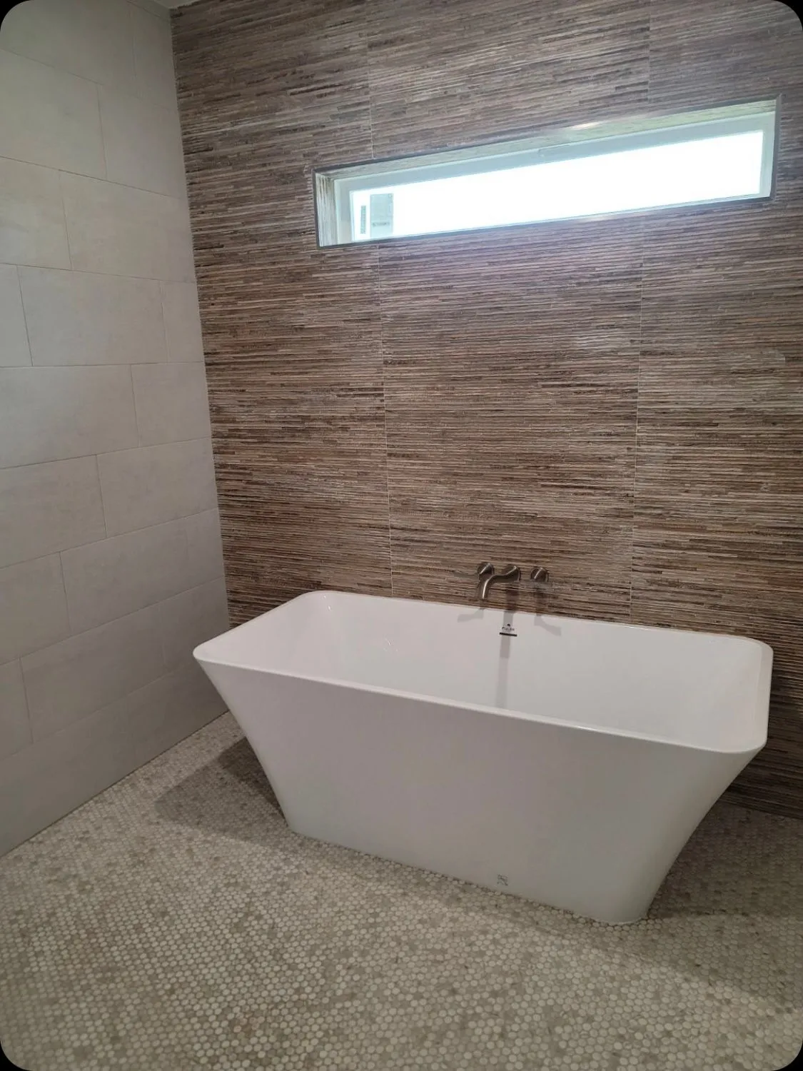 Contemporary freestanding bathtub positioned against textured feature wall highlights sophisticated bathroom remodeling, quality plumbing installation, stylish finishes, premium materials, and exceptional residential bathroom renovation for lasting comfort and beauty.