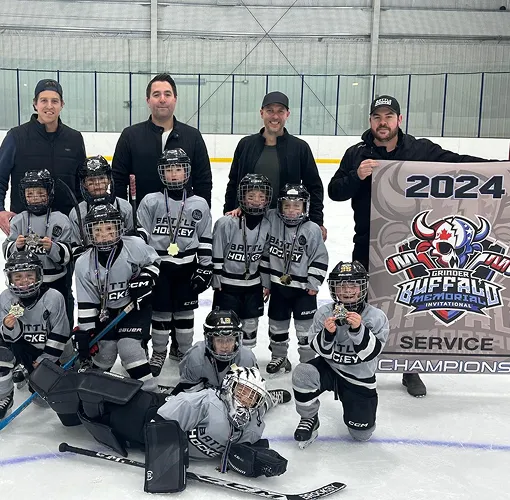 A youth hockey team in full uniforms lined up along the rink boards with coaches behind them.