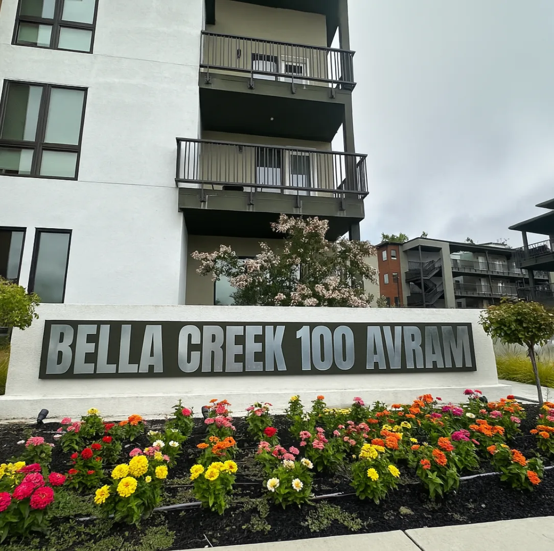 A white building with a sign that says Bella Creek 100 Avram.