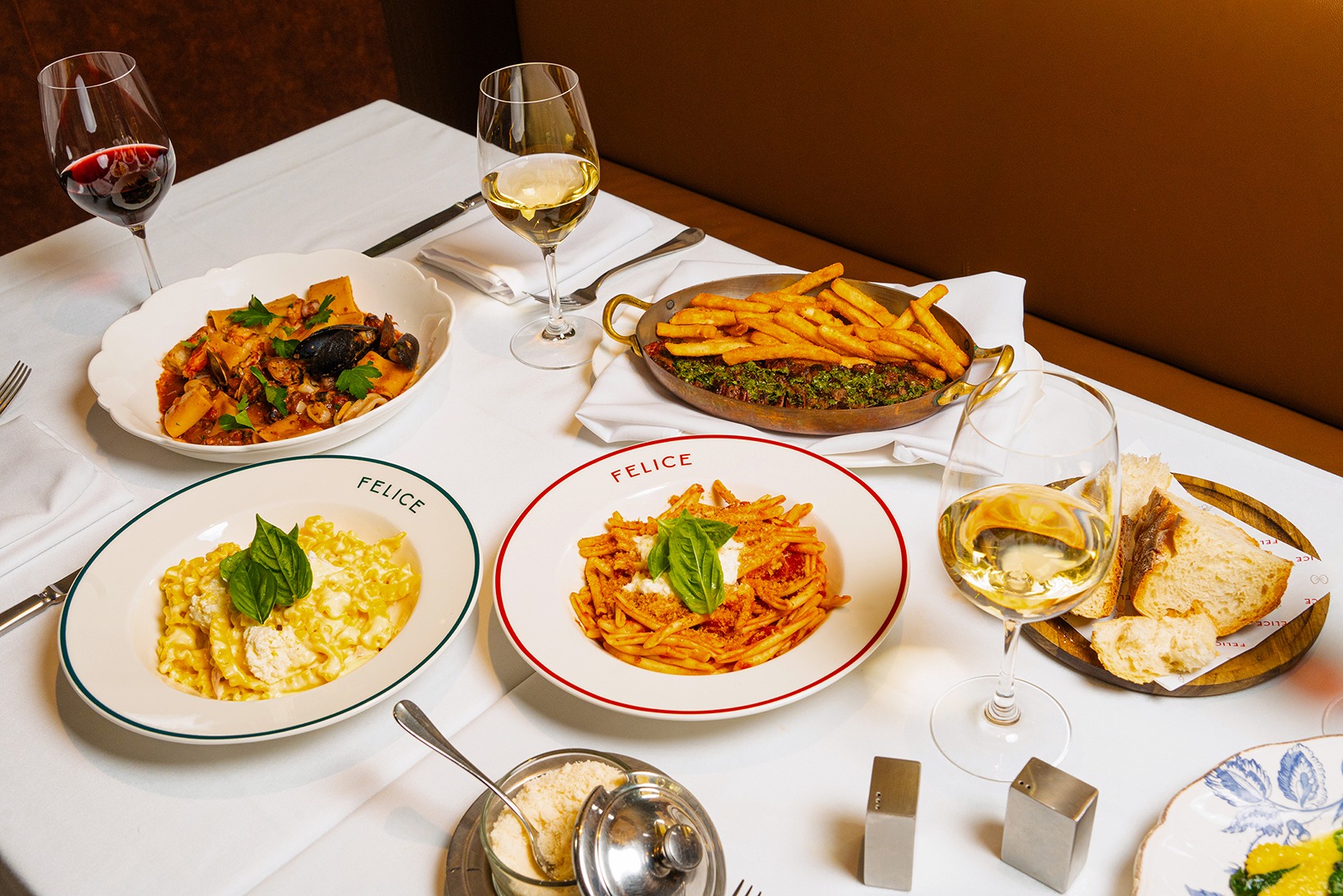 A spread of Italian cuisine including rigatoni seafood pasta, fusilli with tomato and basil, and a side of crispy fries with herb pesto.