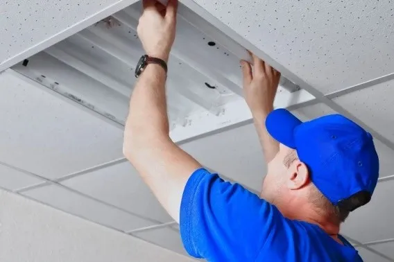 Electrician installing or repairing a commercial ceiling light fixture.