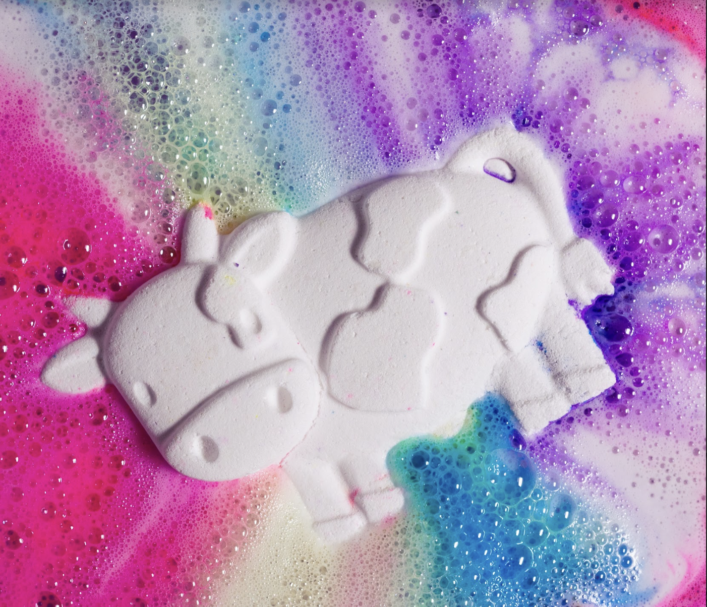 Toby's Magic Cow Bath Bomb in water with rainbow colours effervescing around