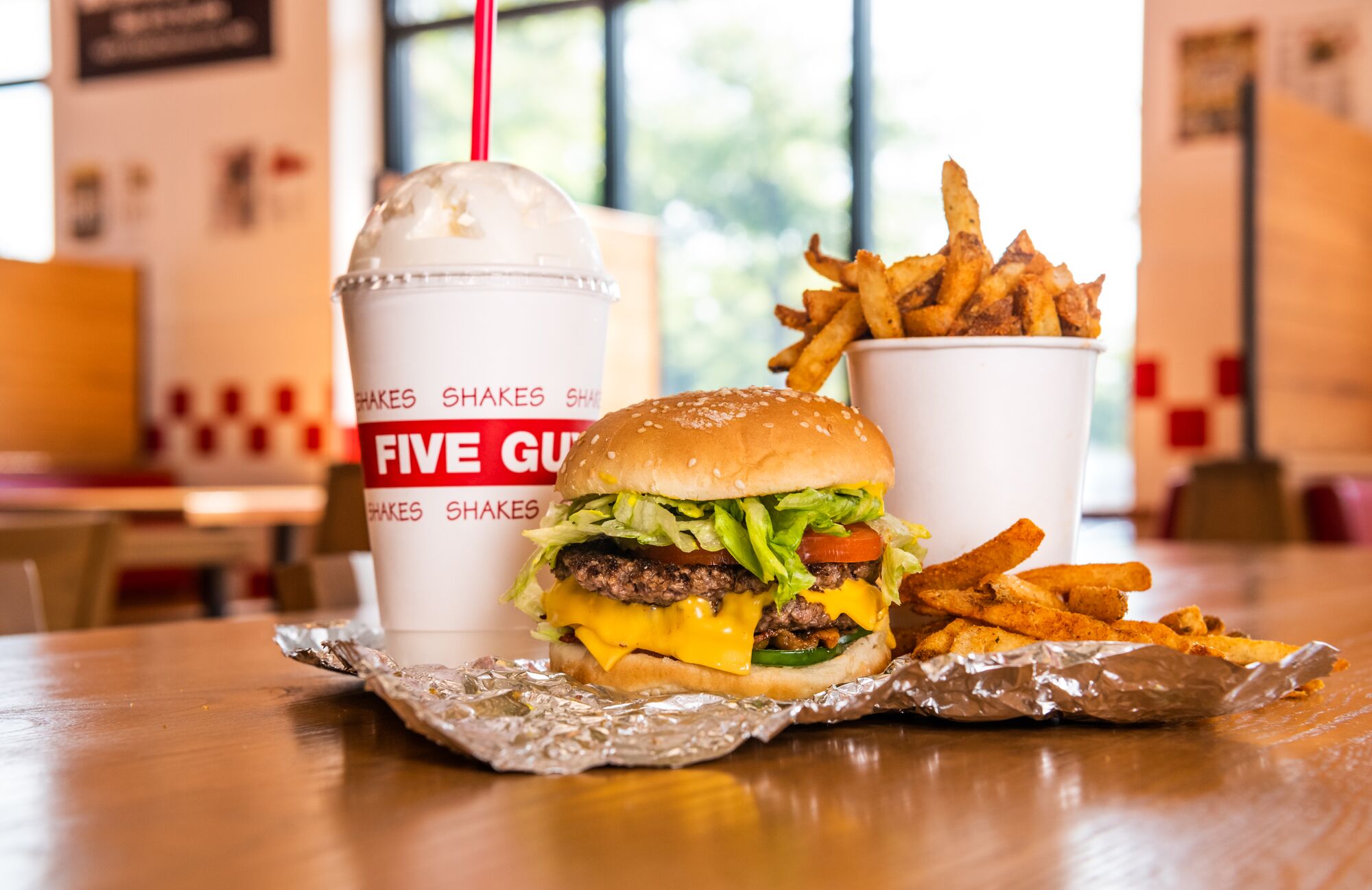 A Five Guys cheeseburger, milkshake and regular order of fries sits on a table inside a Five Guys restaurant.