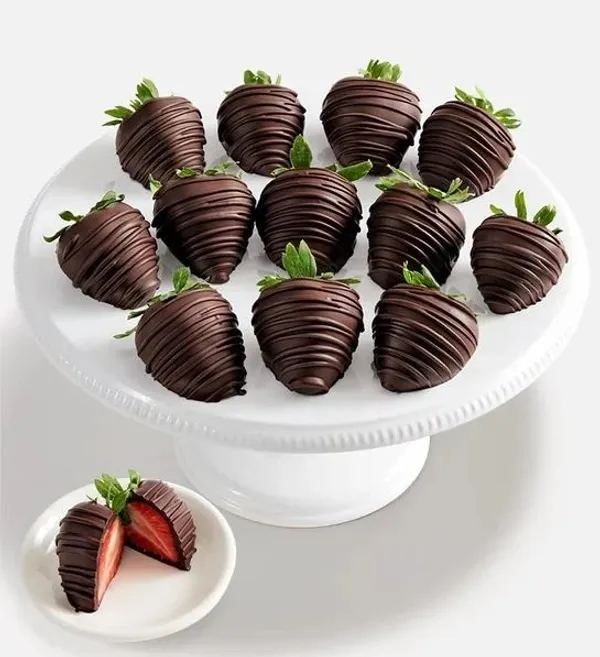 A collection of chocolate-dipped strawberries arranged on a white cake stand. One strawberry is cut  