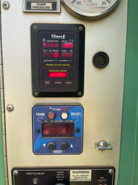 Close-up of vehicle control panel showing Class 1 engine status center, pressure gauge, FoamPro foam system controls, buttons, warning labels, and digital displays mounted on specialized service equipment for operation.