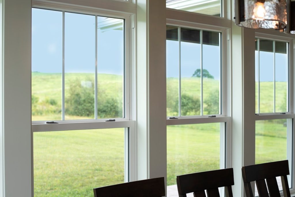 The EcoTek 3200 Series Double-Hung Windows with internal grids frame the outdoor landscape, bringing natural light into the dining room. The clean grid lines add a classic touch to the modern interior, combining elegance with energy efficiency.