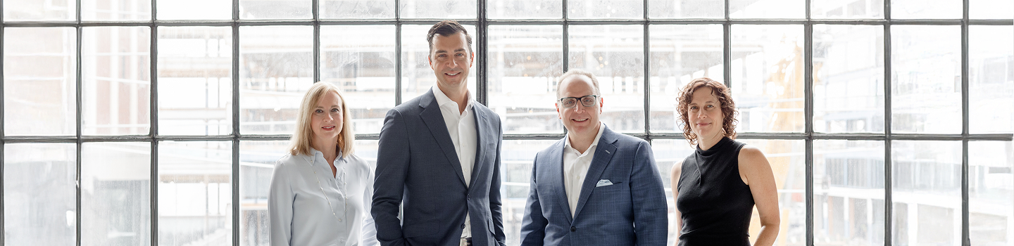 The Barasch - Wellwood team standing side by side in front of a large window.
