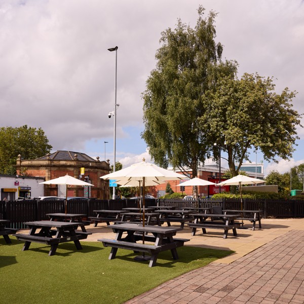 Outdoor beer garden with picnic benches and parasols, perfect for drinks and social gatherings.