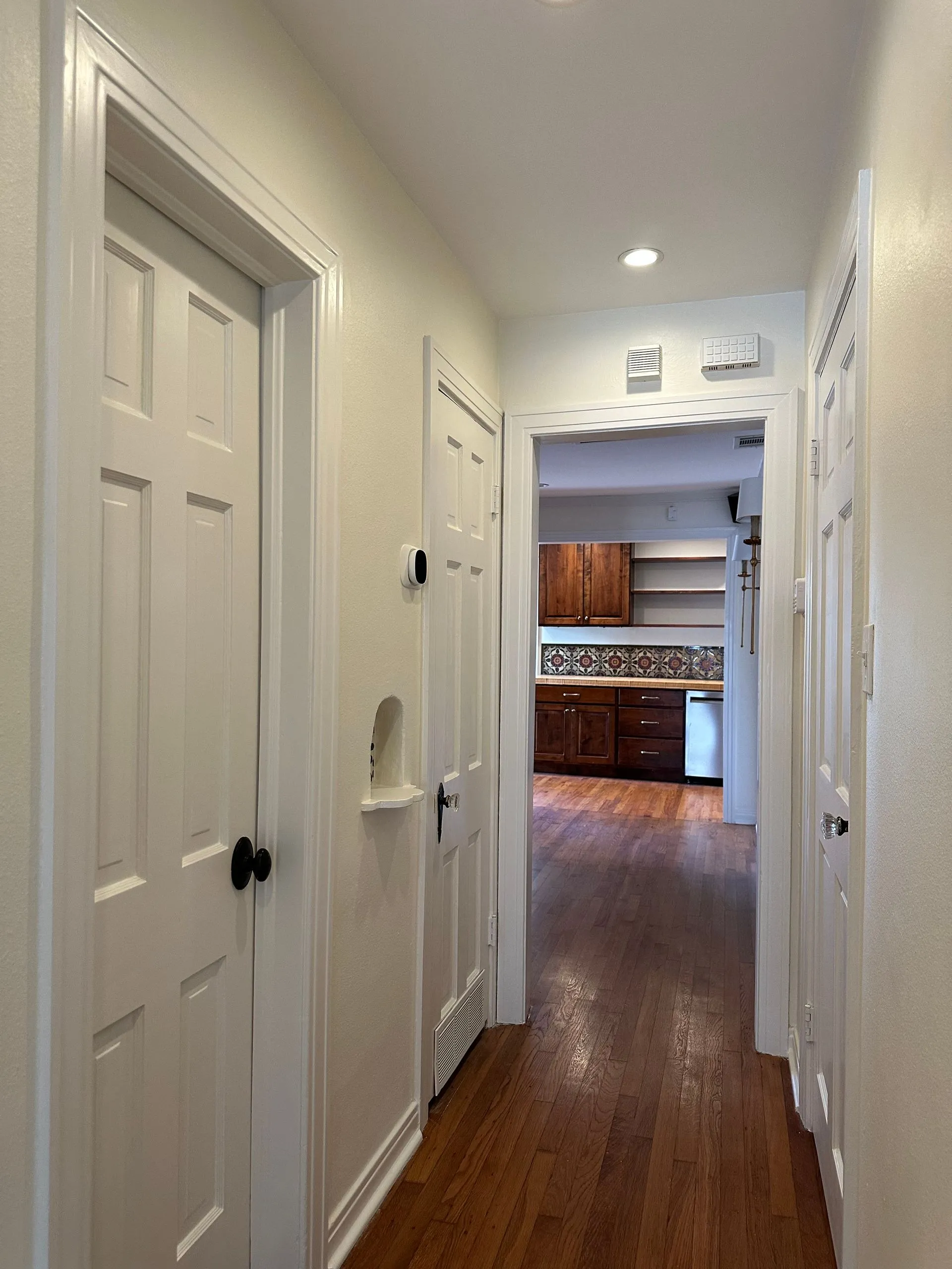 Bright residential hallway features freshly painted walls, updated trim, hardwood flooring, modern l 