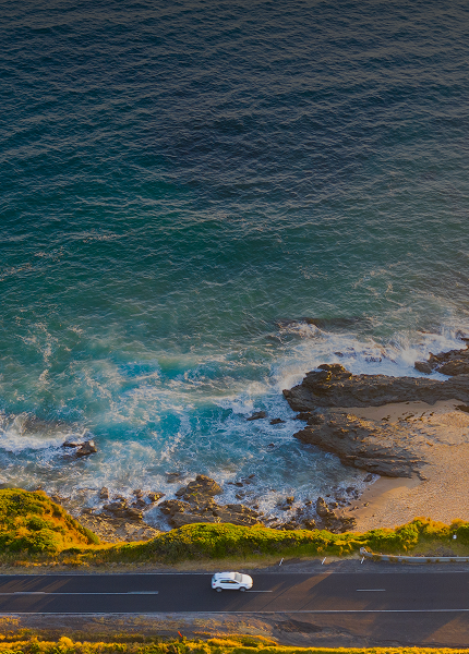 A aerial, top-down view of a coastal highway with waves crashing against the shore.