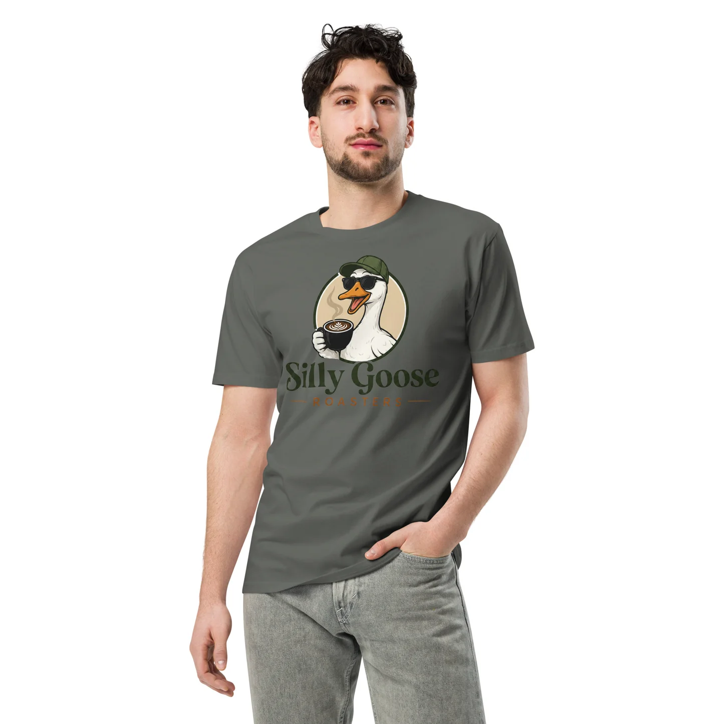 A man in a grey t-shirt with a "Silly Goose" logo featuring a goose wearing sunglasses and holding a coffee cup stands with his hand in his pocket against a white background. The goose is depicted with steam rising from the coffee cup and latte art visible on top. The text "Silly Goose" is prominently displayed below the goose illustration, with "ROASTERS" in smaller text underneath.