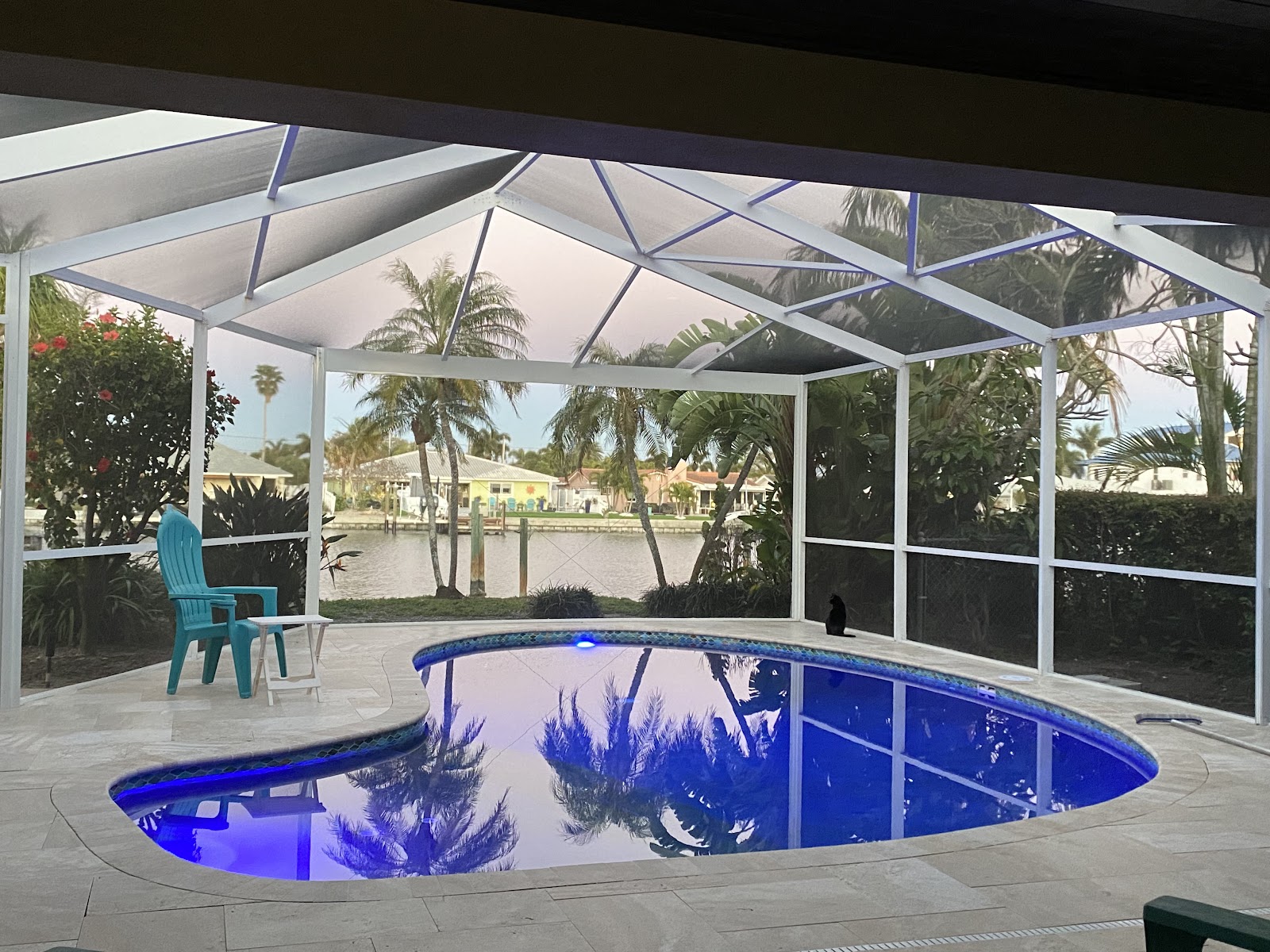 Screen-enclosed residential swimming pool at dusk with blue underwater lighting and a covered patio area.