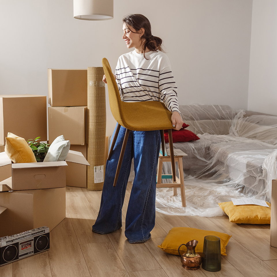 A woman holding a chair in a living room full of boxes