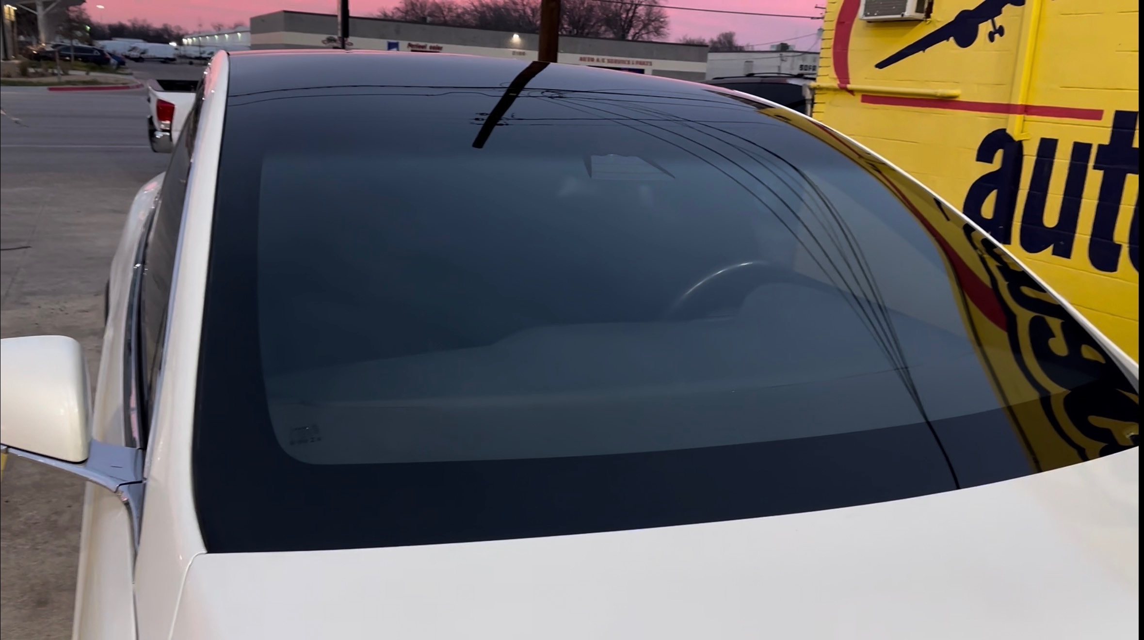 A newly installed windshield is shown on a white vehicle outside the Space Auto Glass shop. The smooth, clear glass demonstrates the finished result of professional windshield replacement service.