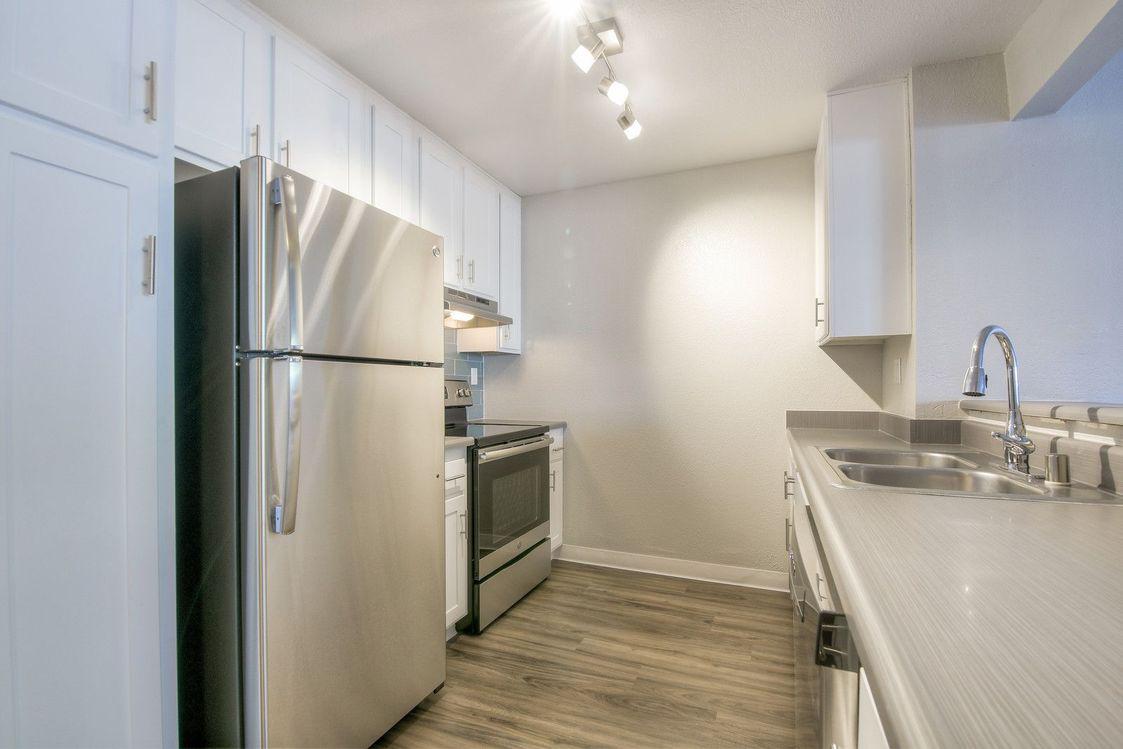 Kitchen with stainless steel appliances, vinyl flooring, and white shaker cabinets.