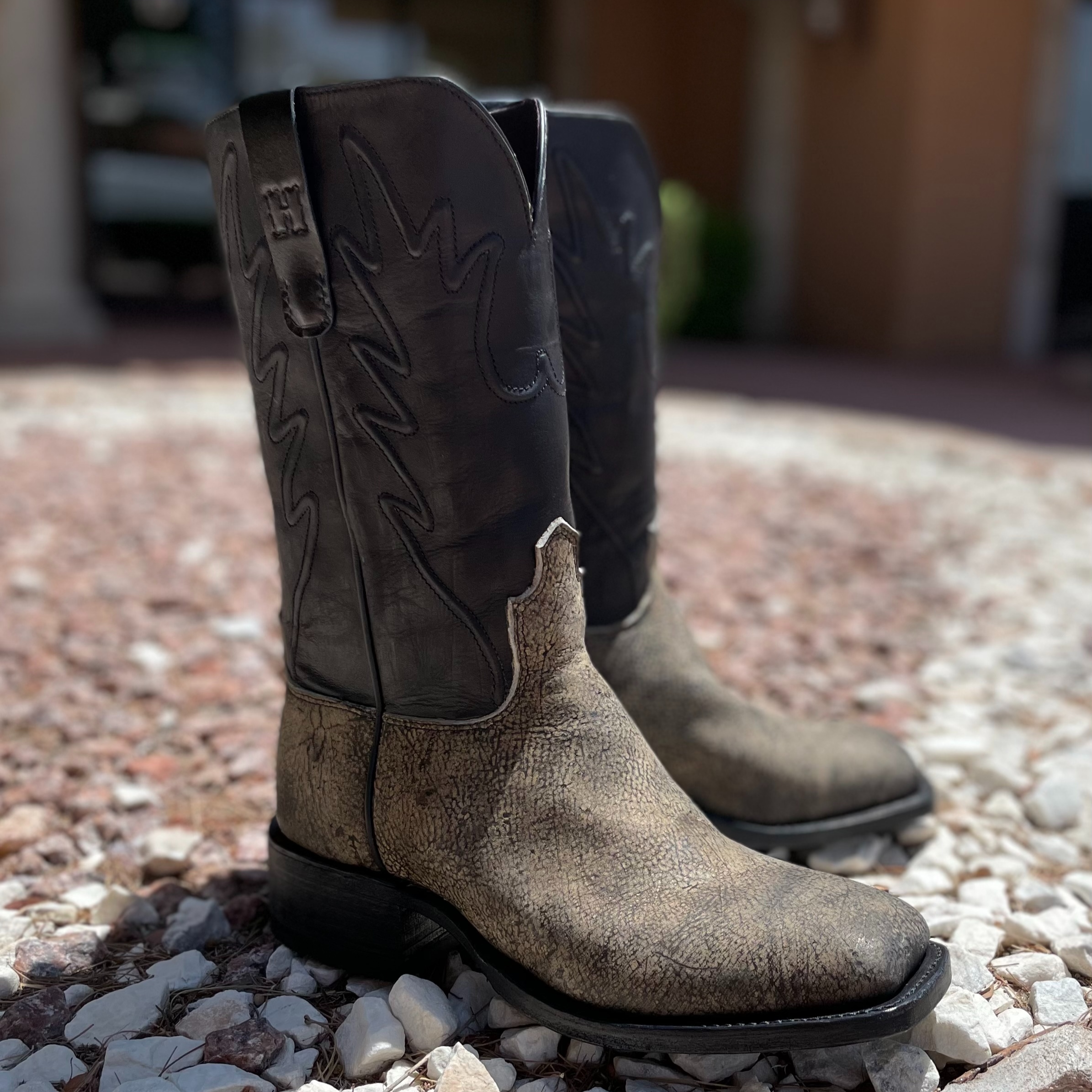 A pair of custom cowboy boots featuring distressed gray leather, black shafts, and understated stitc 