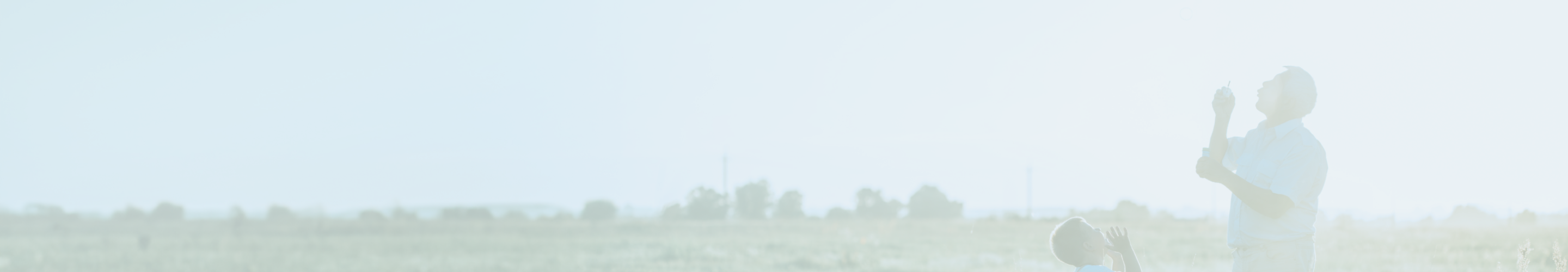 A grandfather and grandchild blowing bubbles in a field.