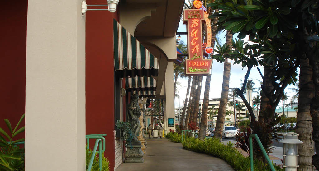 Exterior of Buca di Beppo Honolulu featuring street sign and palm trees in the background.