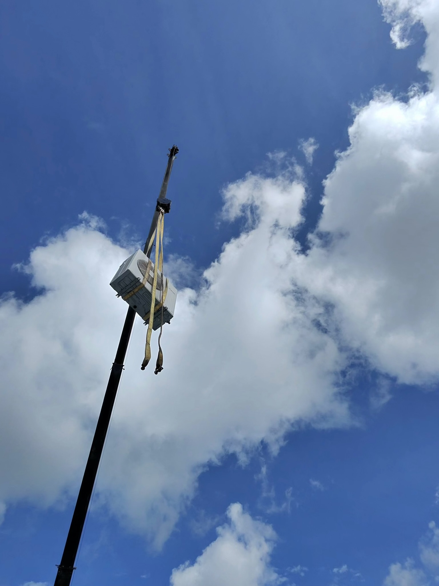 Commercial HVAC equipment is being lifted by crane for safe placement on a building’s rooftop. 