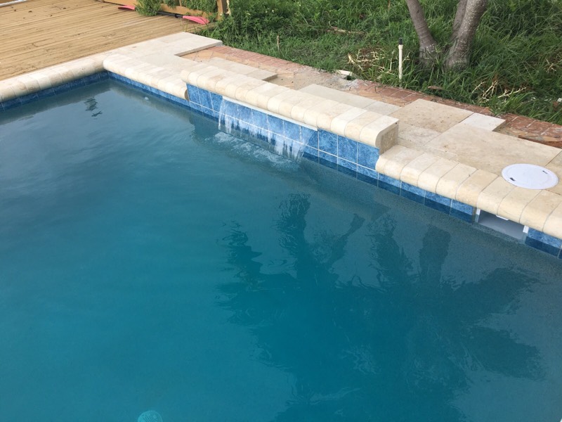 Contemporary residential pool running alongside a multi-story modern home, featuring clear blue water and clean-lined architectural decking.