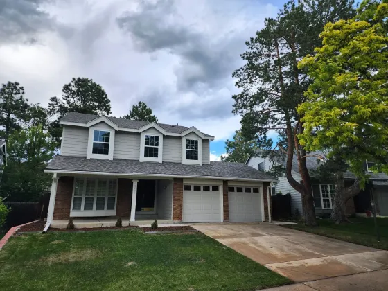 Two-story residential home featuring attached garage, landscaped front yard, mature trees, and attractive curb appeal, representing a property suitable for basement finishing and remodeling projects.