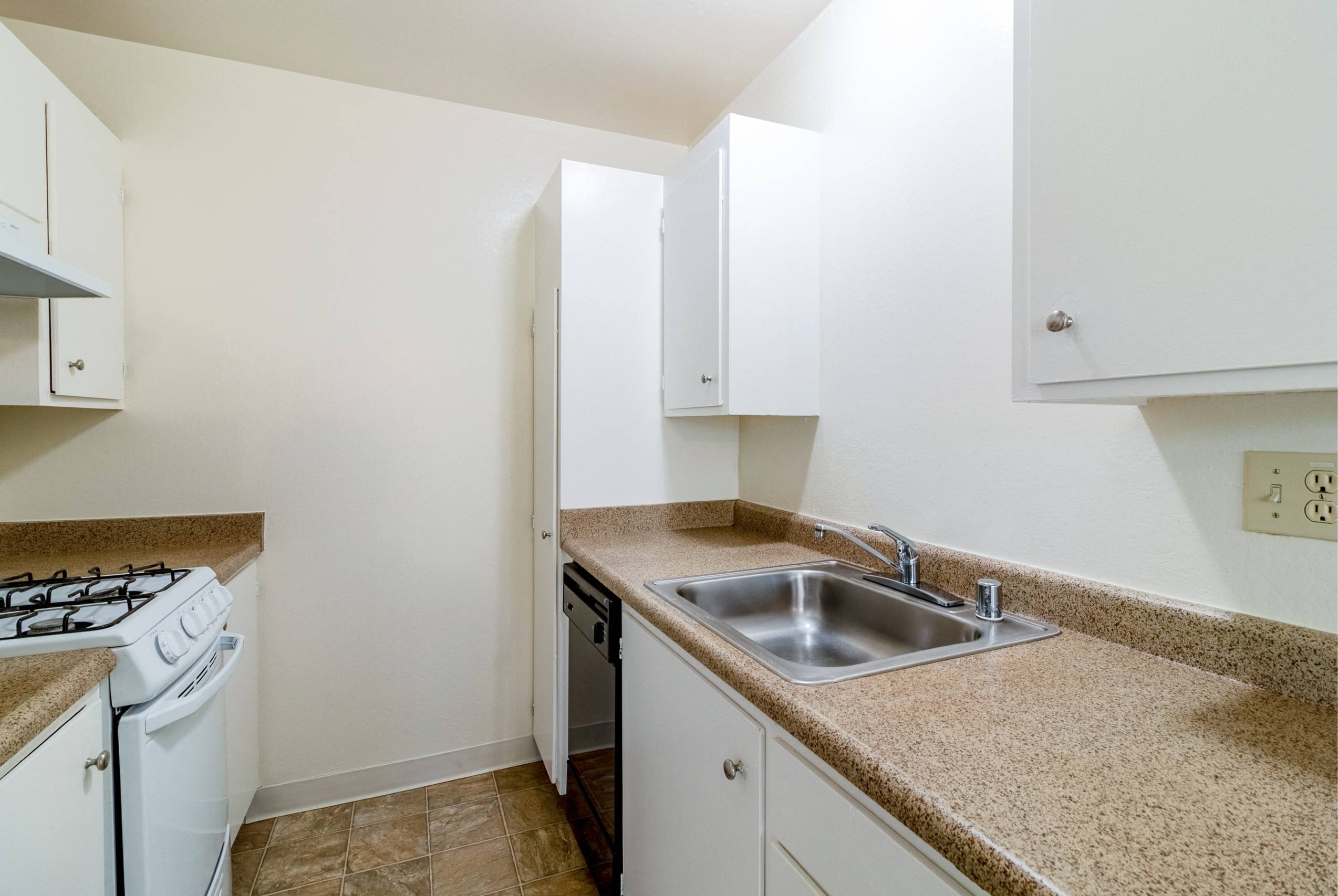 A kitchen with a stove, sink, and cabinets.