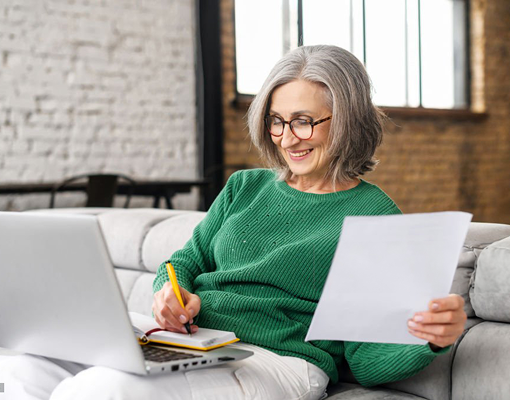 A woman writing notes while looking at a laptop.