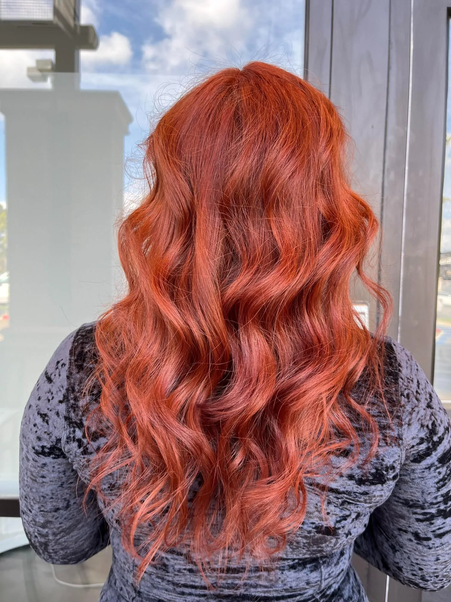 Long copper red hair styled in soft flowing waves, creating rich color dimension and shine. The hairstyle highlights vibrant salon coloring techniques and professional styling photographed from the back.