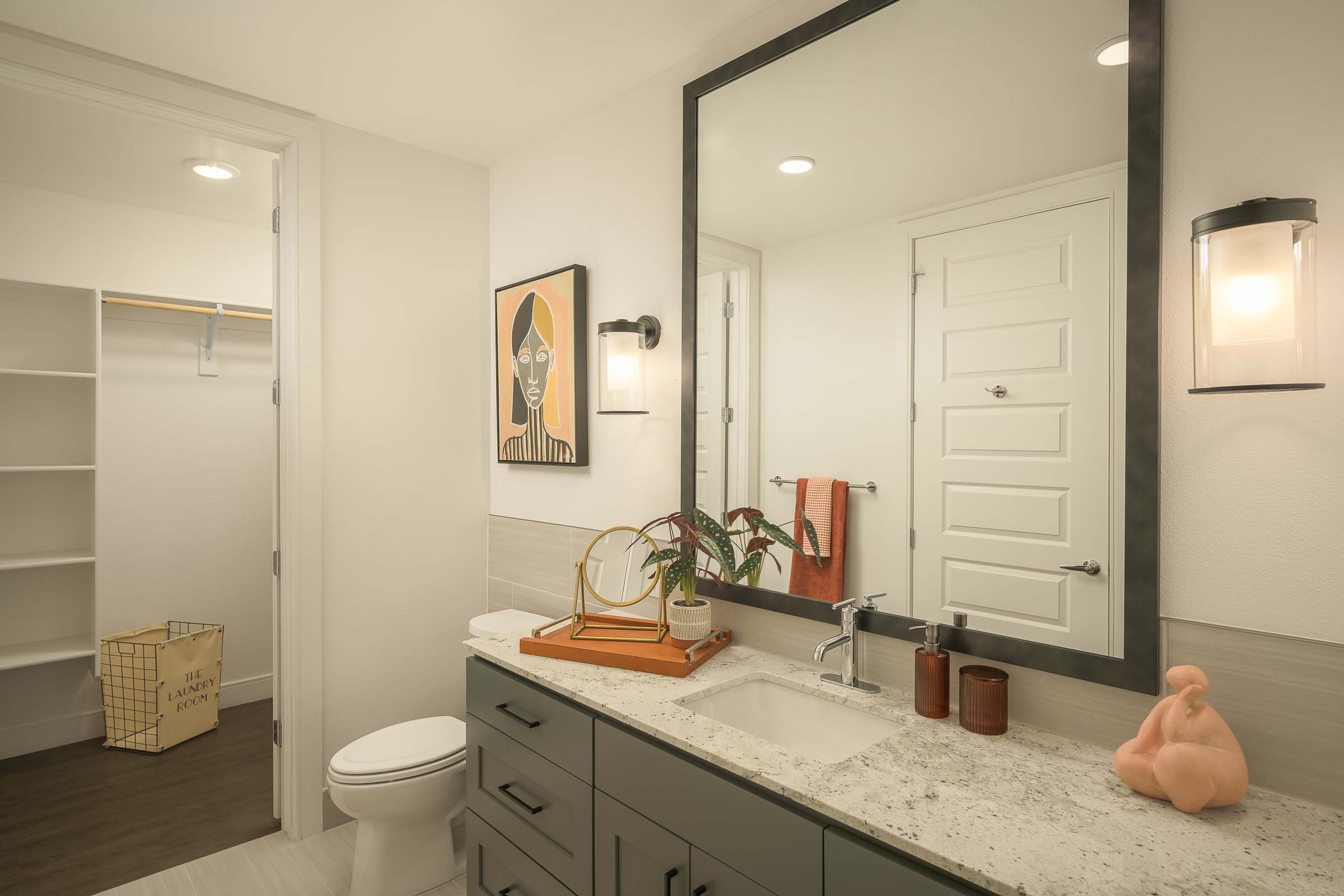 Bathroom with sage green cabinets and open closet with built-in wood shelves at Camden Gilbert apartment homes in Gilbert, AZ