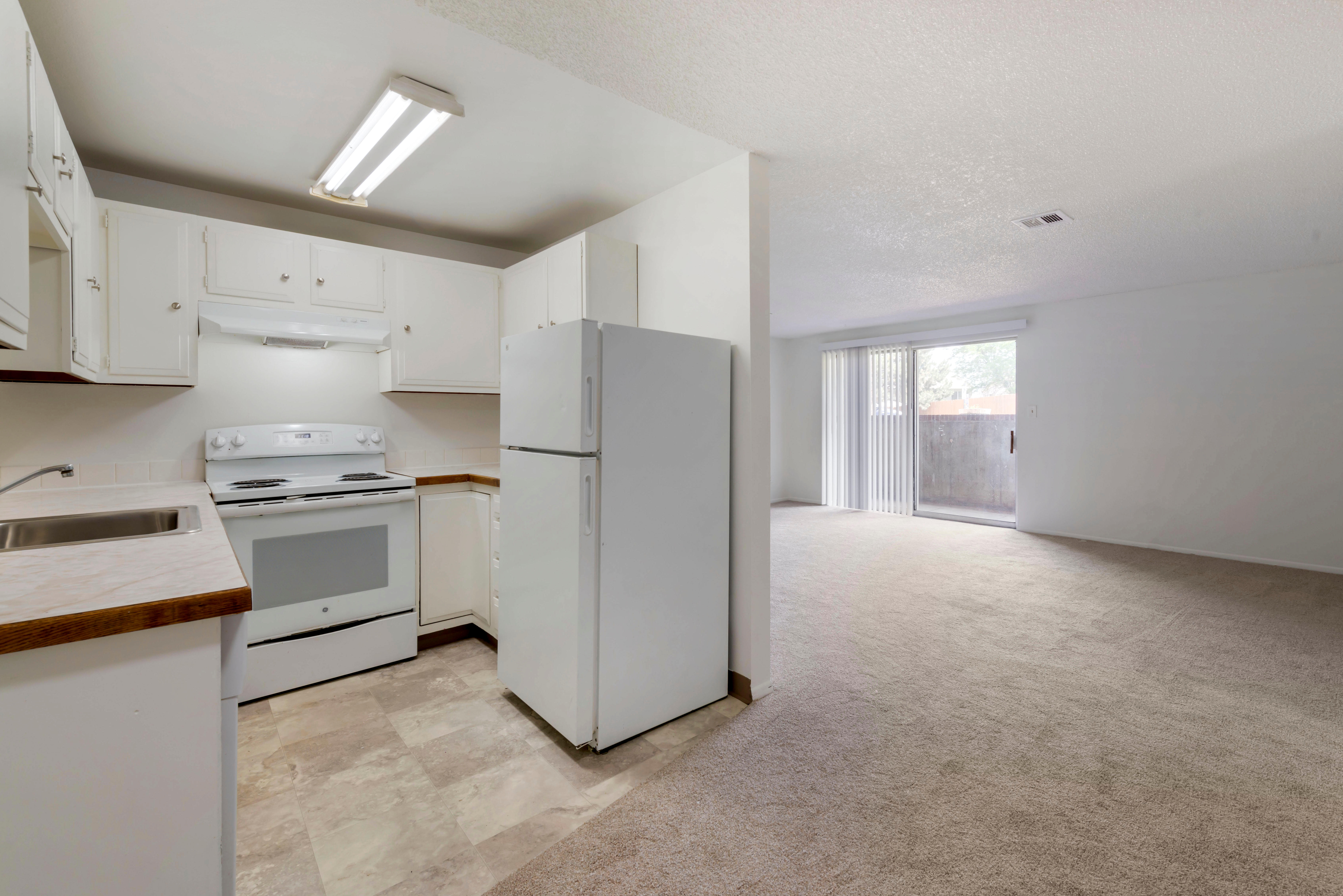 Tile-floored kitchen with white appliances, white cabinets, and view to living room and balcony.