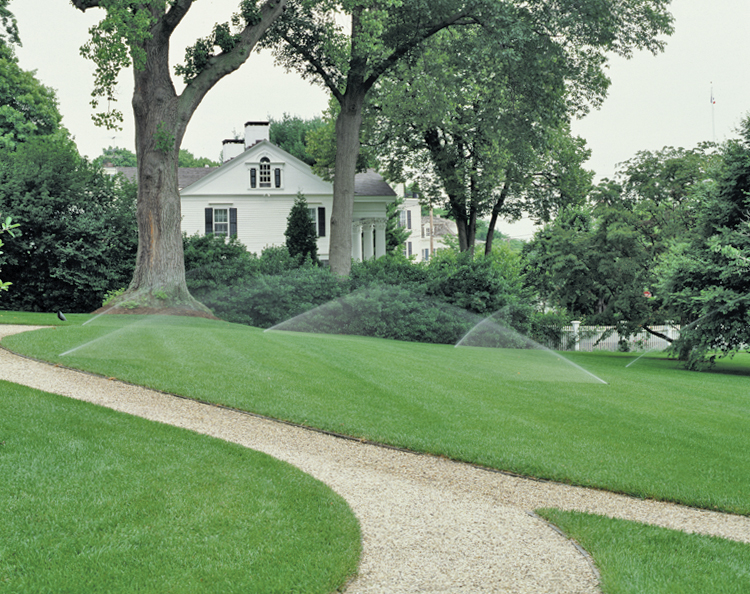 A multi-zone residential irrigation system watering a large, beautifully landscaped green yard and estate lawn.