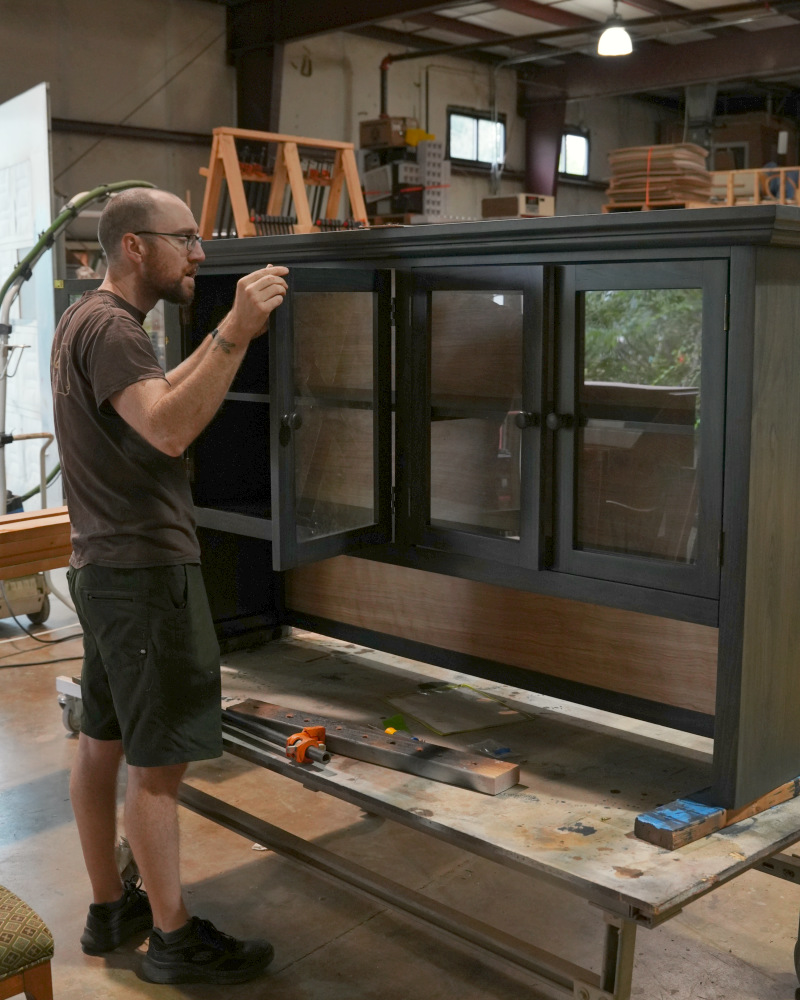 Furniture Restorer Inspecting Finish on Dark Cabinet