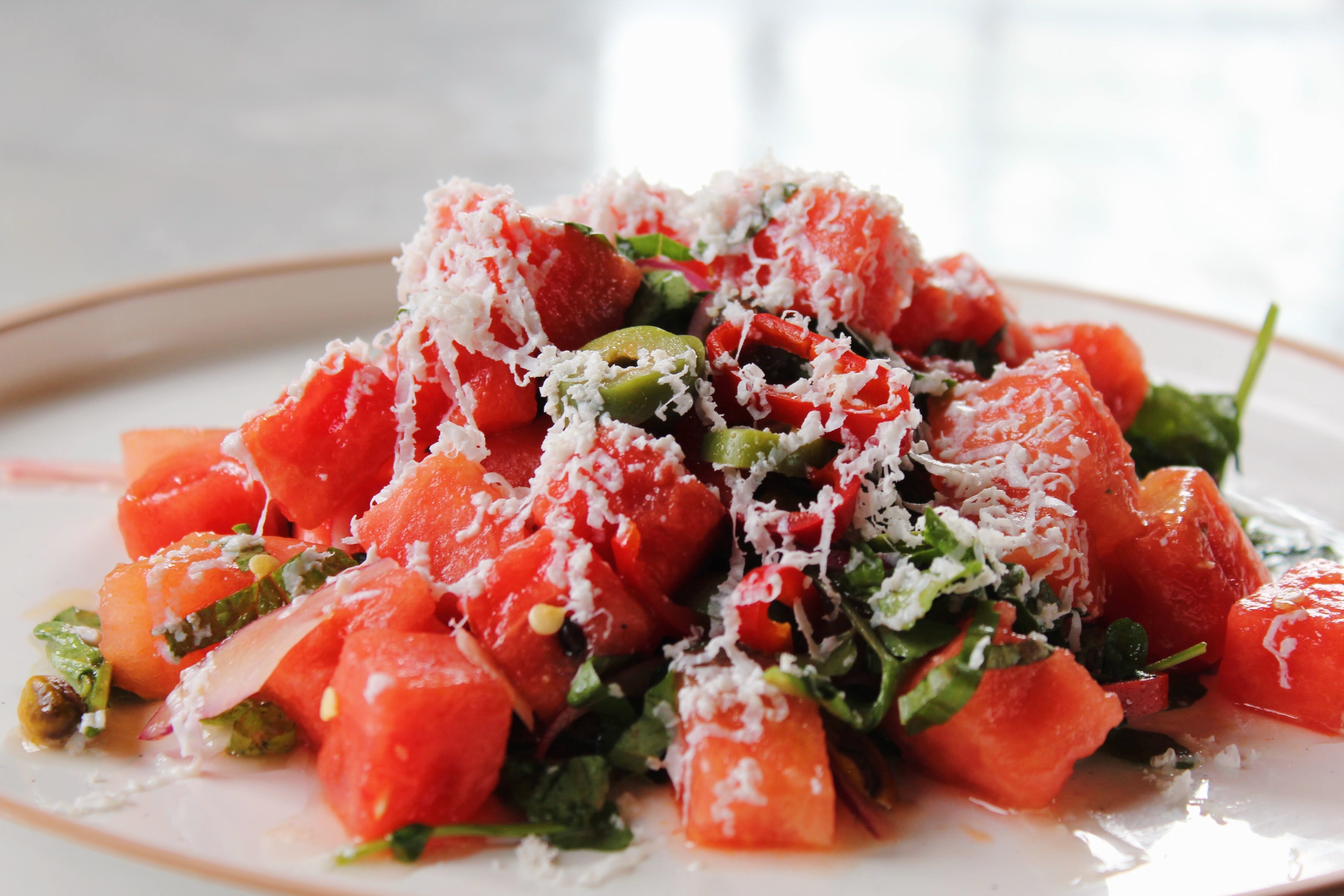 Watermelon Salad — juicy watermelon with watercress, red onions, pickled Fresno chilis, pistachios, Castelvetrano olives, mint, and basil, showered with shaved ricotta salata and citrus vinaigrette.
