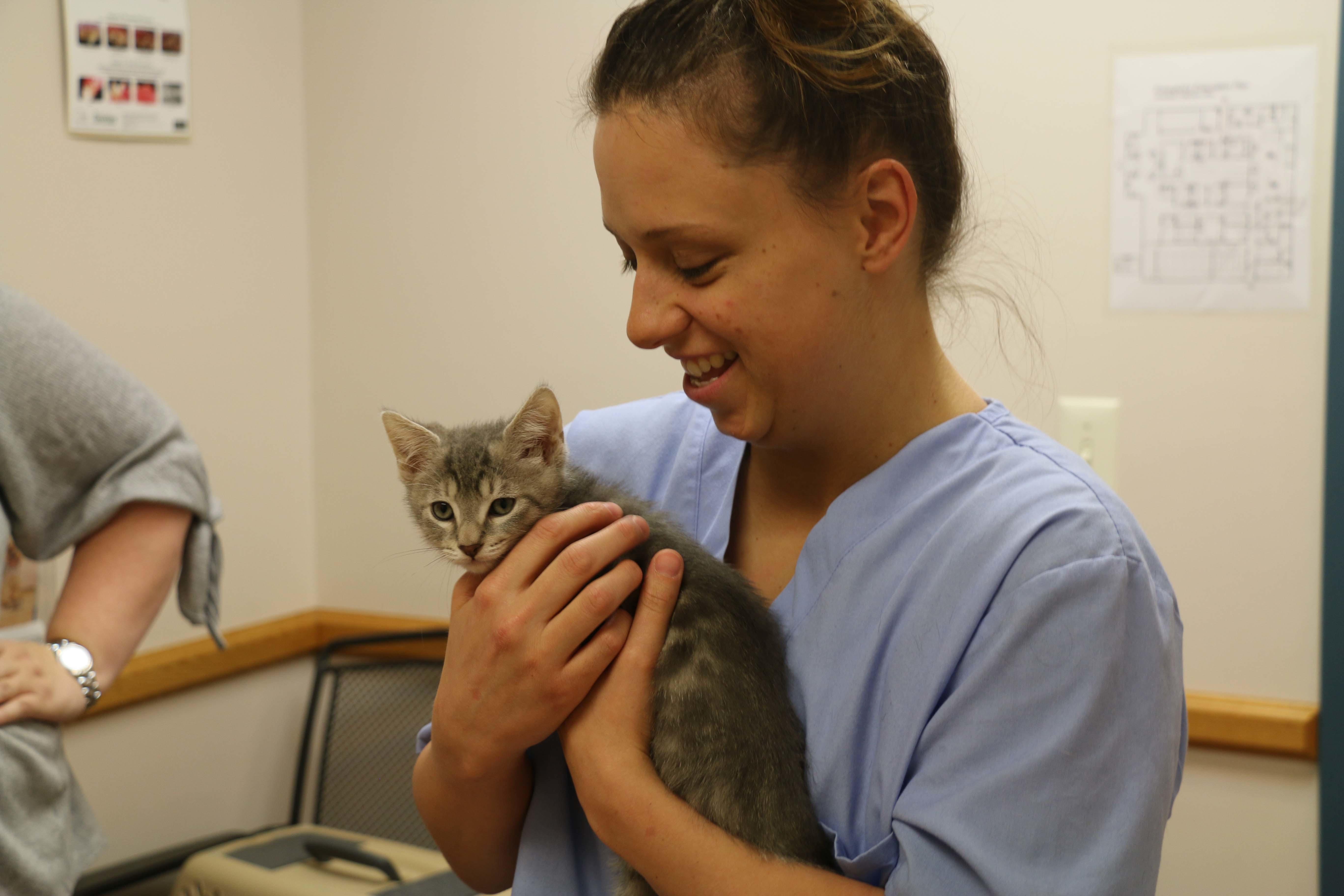 A veterinary technician is all smiles as she cozies up to a new kitten patient.