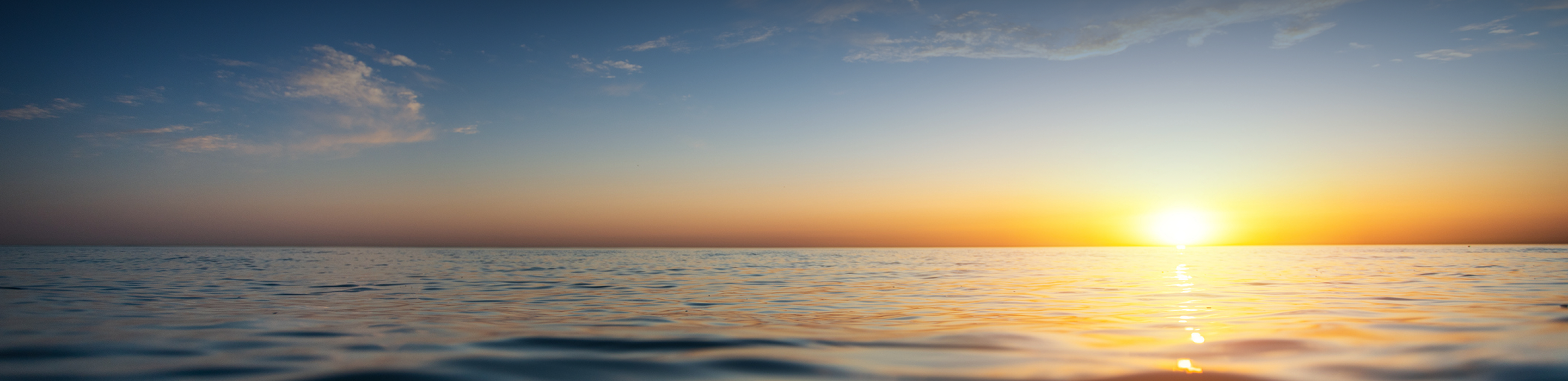 A calm body of water with the setting sun in the background.