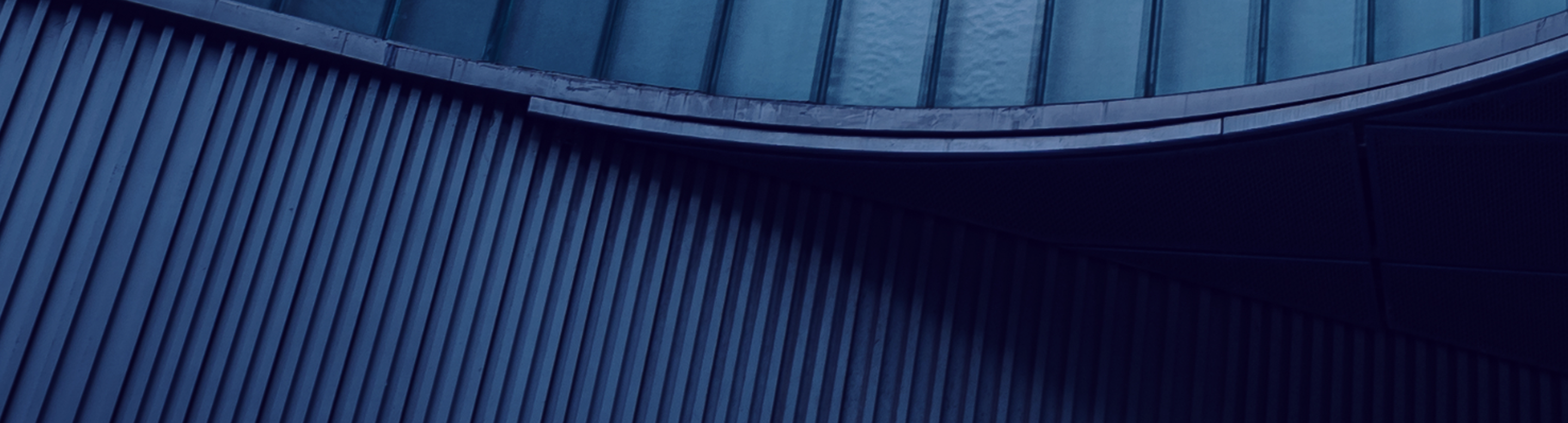 Close-up, abstract image of the exterior of a curved building with multiple levels featuring different vertical lines of varying widths.